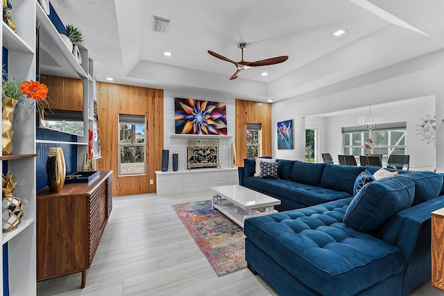 living room with a raised ceiling, a stone fireplace, wooden walls, and a textured ceiling