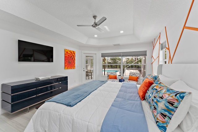 bedroom with ceiling fan, a tray ceiling, access to exterior, and a textured ceiling