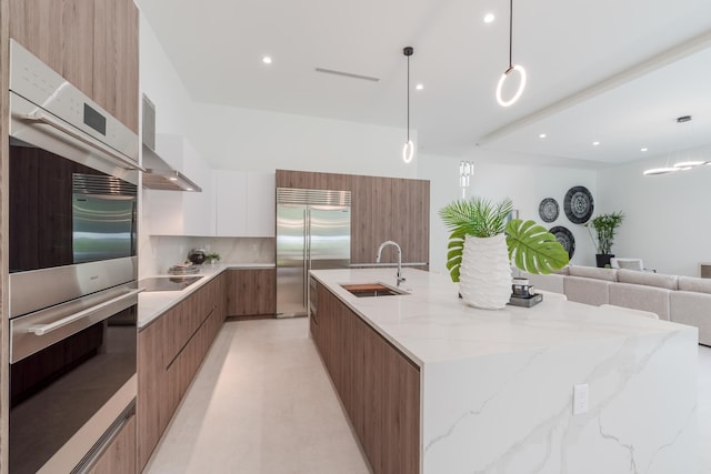 kitchen with wall chimney range hood, sink, hanging light fixtures, stainless steel appliances, and white cabinets