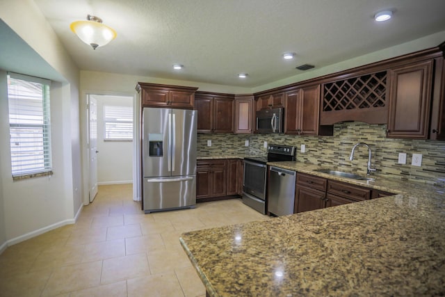 kitchen featuring visible vents, a sink, stone countertops, backsplash, and appliances with stainless steel finishes