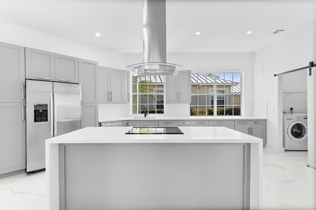 kitchen featuring washer / clothes dryer, stainless steel fridge, a center island, a barn door, and black electric cooktop