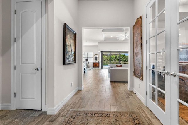 hallway with french doors, baseboards, and light wood finished floors