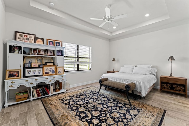 bedroom with baseboards, light wood-style floors, a tray ceiling, and a ceiling fan