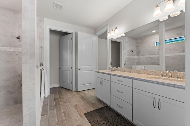 full bathroom featuring visible vents, a sink, wood finished floors, a tile shower, and double vanity