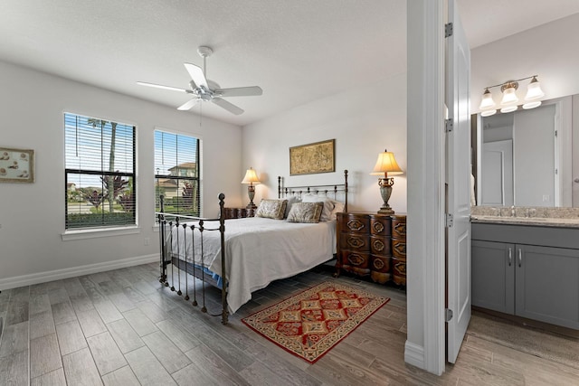 bedroom featuring light wood finished floors, ensuite bath, baseboards, and a sink