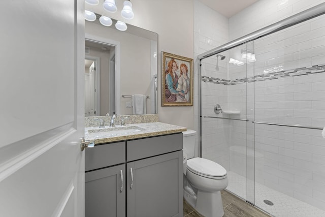 bathroom with vanity, wood finished floors, a shower stall, and toilet