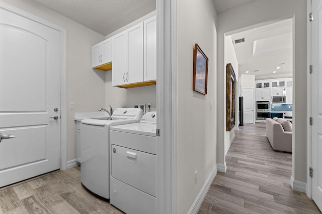 laundry room featuring washing machine and dryer, cabinet space, light wood-style flooring, and visible vents