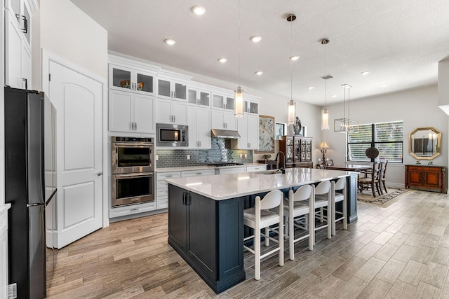 kitchen featuring tasteful backsplash, light wood-type flooring, appliances with stainless steel finishes, white cabinets, and a sink