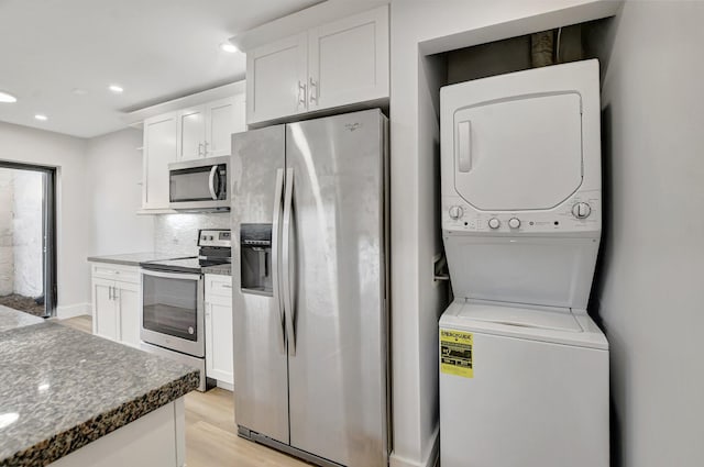 kitchen featuring tasteful backsplash, white cabinetry, stacked washer and clothes dryer, stainless steel appliances, and light hardwood / wood-style flooring