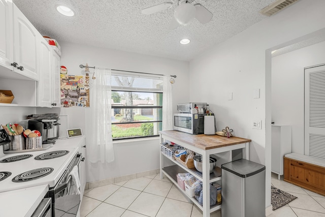 kitchen with electric range oven, light tile patterned floors, white cabinets, and a textured ceiling