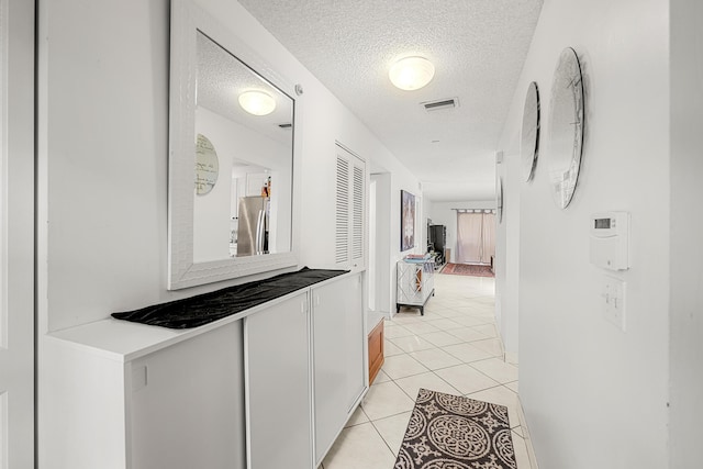 hallway with a textured ceiling and light tile patterned floors