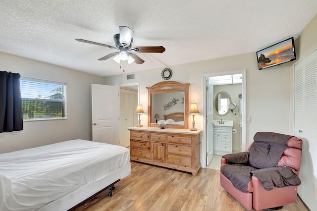 bedroom with a textured ceiling, ensuite bathroom, a sink, visible vents, and light wood-type flooring