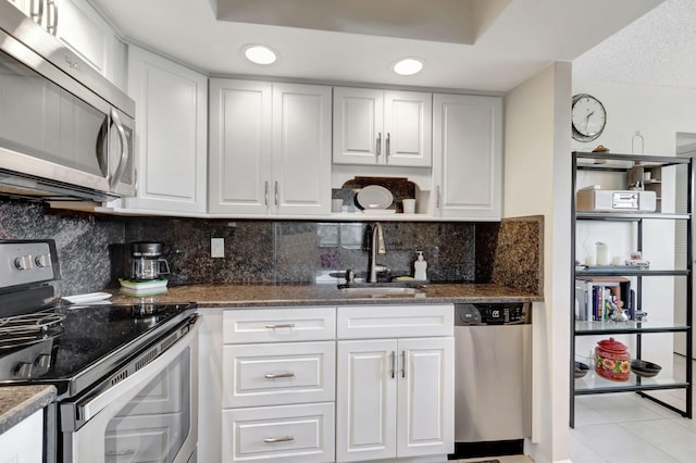 kitchen featuring white cabinets, dark stone countertops, stainless steel appliances, and a sink