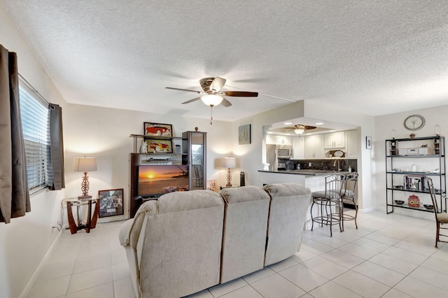 living area with light tile patterned floors, ceiling fan, baseboards, and a textured ceiling