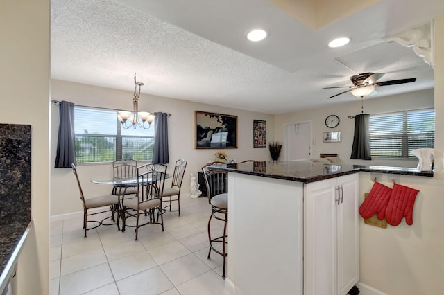 kitchen with a textured ceiling, a peninsula, white cabinetry, a kitchen breakfast bar, and decorative light fixtures