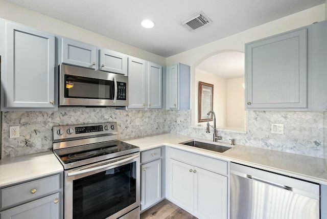 kitchen with stainless steel appliances, sink, light hardwood / wood-style floors, and decorative backsplash