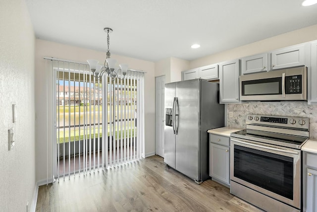 kitchen with light hardwood / wood-style flooring, gray cabinetry, hanging light fixtures, stainless steel appliances, and tasteful backsplash