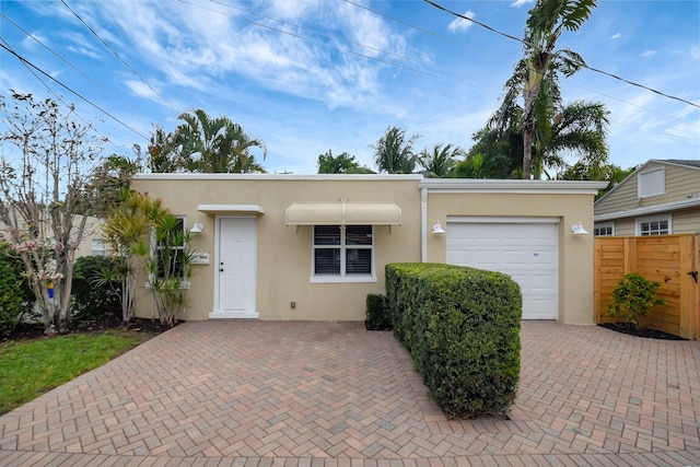 view of front of property with decorative driveway, an attached garage, fence, and stucco siding