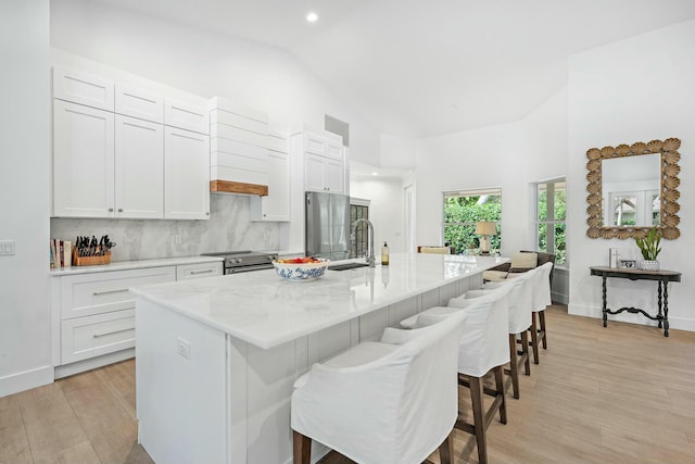 kitchen featuring a kitchen island with sink, stainless steel appliances, white cabinets, and a kitchen bar