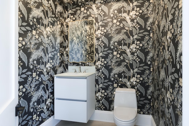 half bathroom featuring baseboards, vanity, toilet, and wallpapered walls