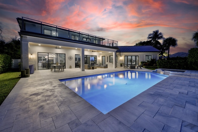 back of property at dusk with a patio, a balcony, a standing seam roof, outdoor dining area, and stucco siding