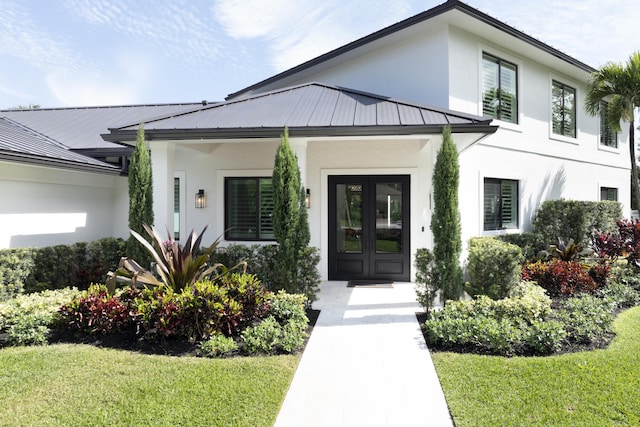 property entrance with french doors, stucco siding, a lawn, a standing seam roof, and metal roof