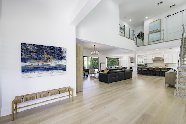 living room featuring a notable chandelier, a towering ceiling, visible vents, and light wood-style floors