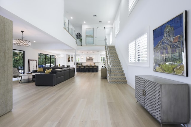 living area with a barn door, recessed lighting, a high ceiling, light wood-style floors, and stairs