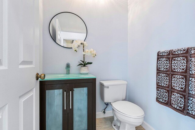 half bathroom with toilet, baseboards, and vanity