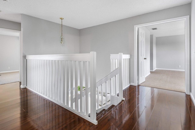 corridor featuring visible vents, dark wood-type flooring, an upstairs landing, and baseboards