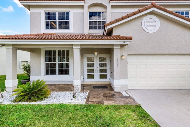 view of front of property with french doors, a tile roof, an attached garage, and stucco siding