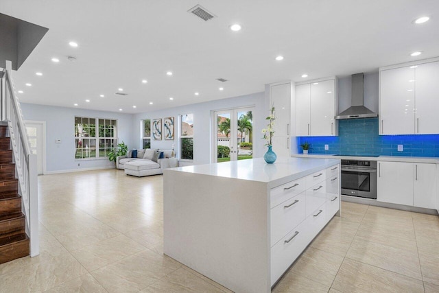 kitchen featuring light countertops, visible vents, white cabinetry, stainless steel oven, and wall chimney exhaust hood