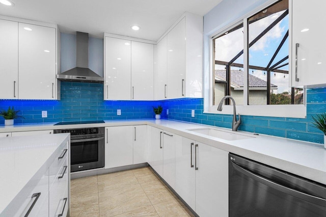 kitchen featuring dishwashing machine, oven, white cabinetry, light countertops, and wall chimney range hood