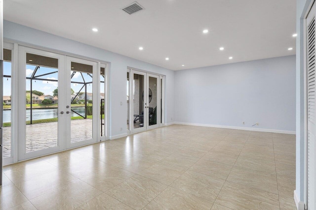 empty room with french doors, a water view, visible vents, and baseboards