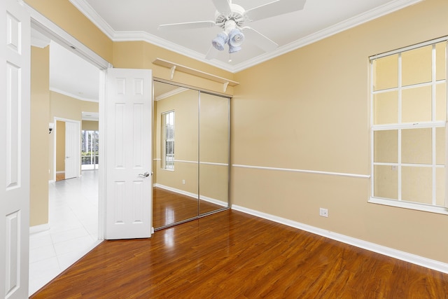 unfurnished bedroom with crown molding, ceiling fan, wood-type flooring, and a closet