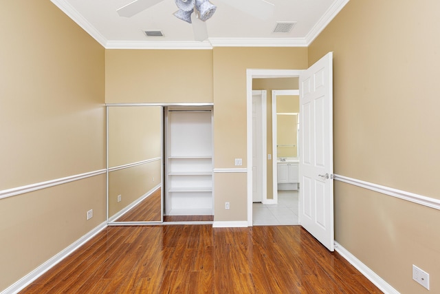 unfurnished bedroom featuring hardwood / wood-style flooring, crown molding, ceiling fan, and a closet