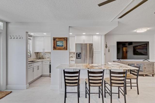 kitchen with a breakfast bar, white cabinets, backsplash, light stone countertops, and stainless steel fridge