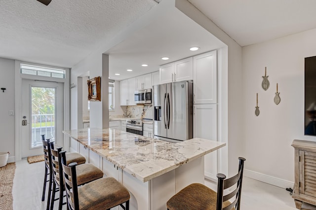 kitchen with appliances with stainless steel finishes, a kitchen bar, white cabinetry, and light stone countertops