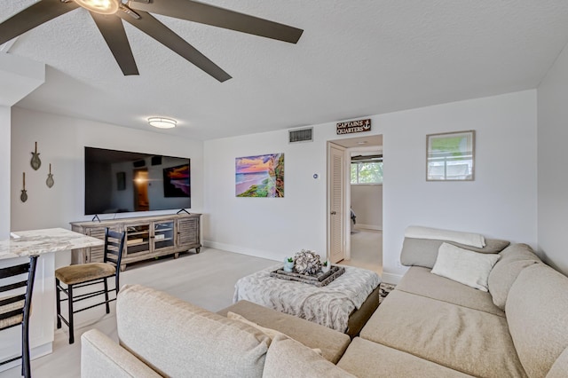 living room featuring a textured ceiling, a ceiling fan, visible vents, and baseboards