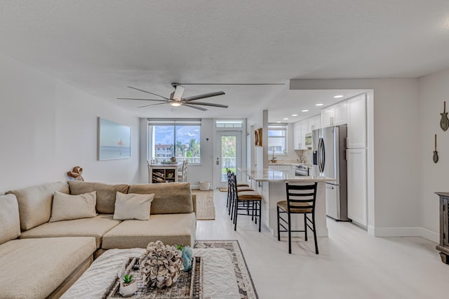 living room featuring baseboards, a ceiling fan, a textured ceiling, light wood-style floors, and recessed lighting