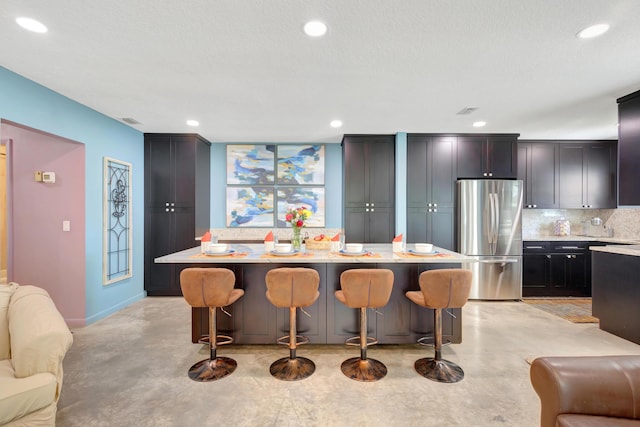 kitchen featuring a kitchen island, backsplash, stainless steel fridge, a kitchen breakfast bar, and light stone countertops