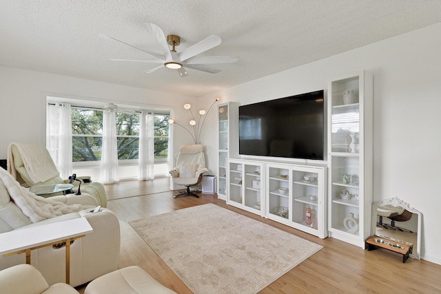 living room featuring ceiling fan, light hardwood / wood-style floors, and a textured ceiling