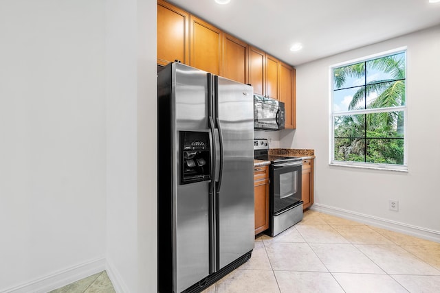 kitchen with light tile patterned flooring, dark stone counters, and appliances with stainless steel finishes