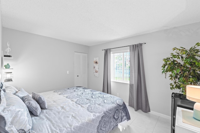 bedroom featuring light tile patterned floors, baseboards, and a textured ceiling