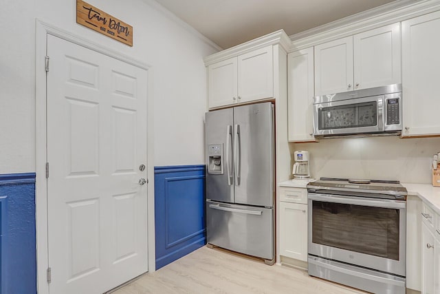 kitchen featuring light wood-type flooring, ornamental molding, white cabinets, and appliances with stainless steel finishes