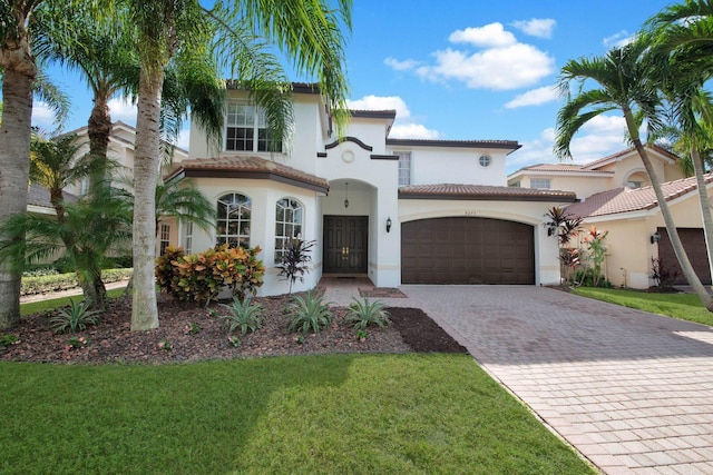 mediterranean / spanish house featuring stucco siding, decorative driveway, a front yard, a garage, and a tiled roof