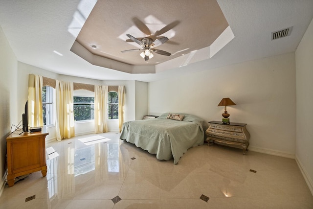 bedroom featuring a tray ceiling, baseboards, visible vents, and a ceiling fan