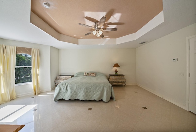 bedroom with light tile patterned floors, a tray ceiling, baseboards, and visible vents