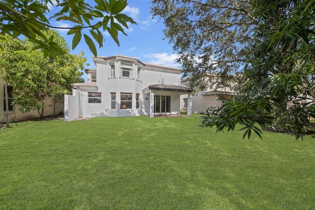 back of house featuring a lawn, a tile roof, and stucco siding