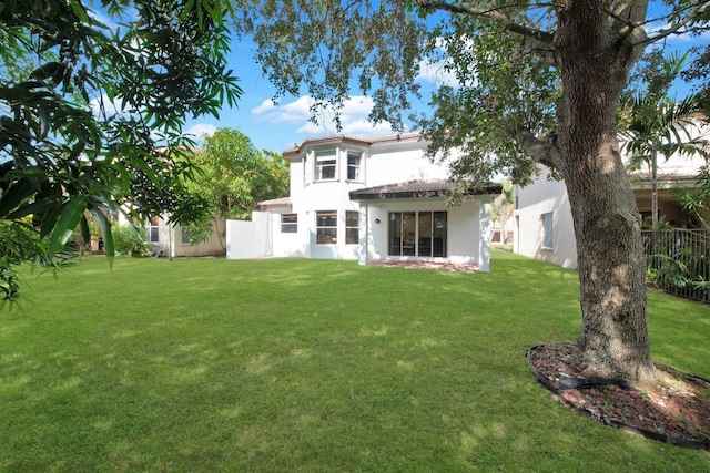 rear view of property with a yard, fence, stucco siding, and a tiled roof